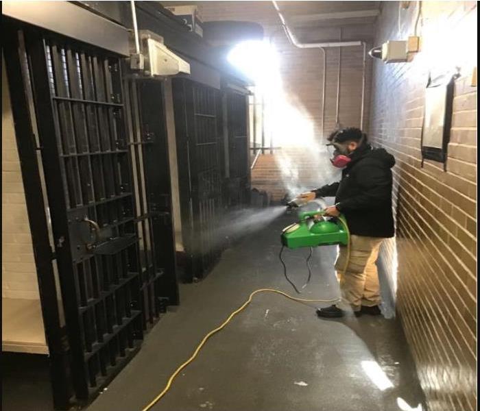 techncian applying disinfecting spray in the holding area of a police department